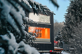 Ein Tiny House steht im Wald, die Bäume sind mit Schnee bedeckt.